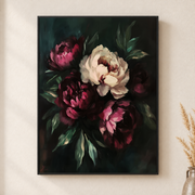 Framed canvas wall art depicting blush peonies and dark burgundy flowers rising from dense green foliage on a neutral wall
