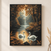 Framed canvas wall art depicting two white swans gliding across a golden forest lake in evening light on a neutral wall